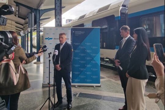 Fotografija iz novinarske konference, predstavniki SŽ in Direkcije za infrastrukturo na peronu, v ozadju vlak Stadler Flirt.